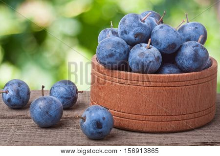 blackthorn berries in a wooden bowl on a table with blurred background.