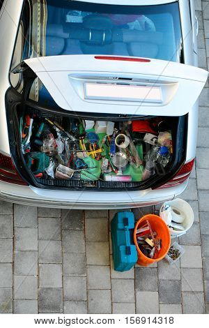 Open car trunk baggage compartment loaded with old work tools and junk on grey paving stone background