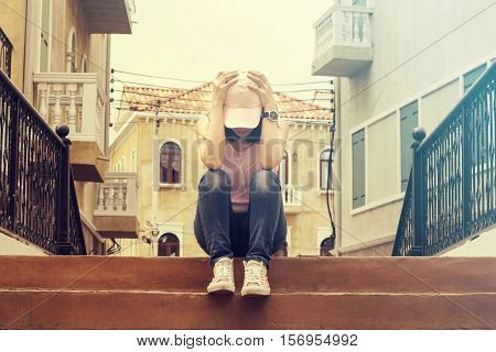 sad woman wearing a cap and hugging knees on stair she is lonely most of the time vintage tone