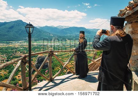 Trikala Meteora Greece - May 25 2015: The priest takes a picture of another priest on the lookout of The Holy Monastery of Great Meteoron against the Thessalian valley, Meteora, Trikala, Greece