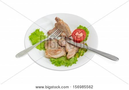 Three slices of fried pork neck on lettuce leaves slices of tomato and green chili fork and knife on white dish on a light background
