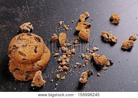 Tasty cookies with chocolate chips and crumbs on dark background