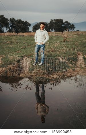 Attractive guy with jeans and white jersey next to a river in the meadow