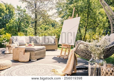 Mockup Of Easel On Terrace In The Garden With Rattan Table And Sofa During Summer. Real Photo