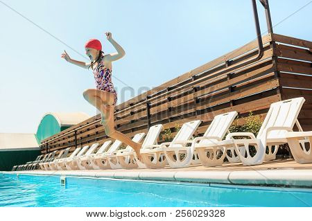 The Portrait Of Happy Smiling Beautiful Teen Girl Jumping At The Swimming Pool. Little Child At Blue