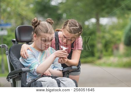A Young Girl Helping Her Disabled Sister In A Wheelchair