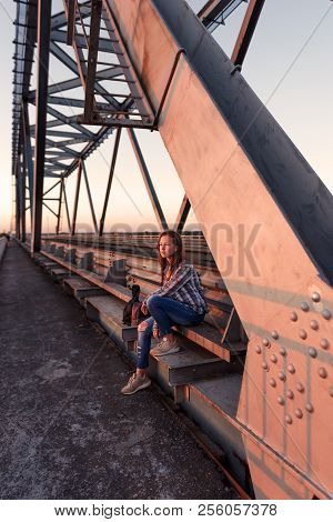 Teen Girl Rebellious Lonely Pensively Sits On Parapet Of Steel Bridge Construction In Abandoned Dock