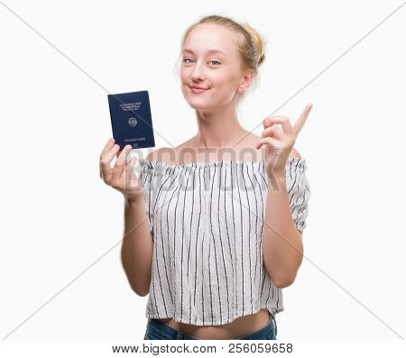 Blonde teenager woman holding passport of Germany surprised with an idea or question pointing finger with happy face, number one