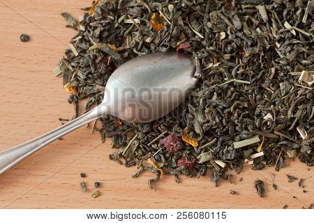 Background With Green Tea. Dried Green Tea Leaves On The Table. Spilled Tea Leaves And A Teaspoon.