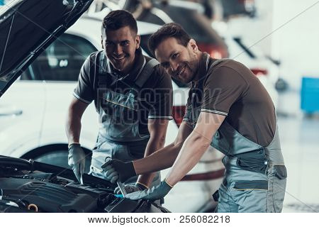 Two Mecanics Looking At Camera While Fixing Car. Portrait Of Caucasian Handsome Happy Workers In Uni