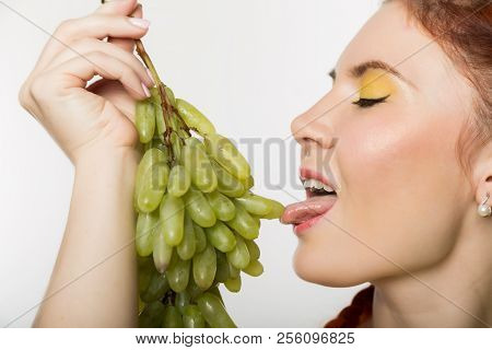 Beautiful Redhead Woman Licks Grapes. Concept Of Healthy Eating