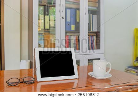 Mock Up Image Of White Tablet Pc With Black Blank Screen And Coffee Cup On Wooden Table In Blur Offi