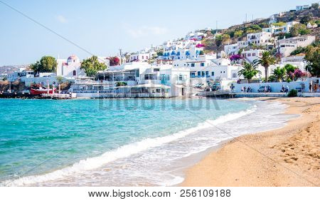 Awesome scenery of tranquoise seacoast and sandy beach with nice white buildings on mountanious greece island resort on the background