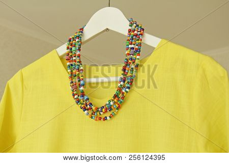 Bright Beads Of Murano Glass Hang On The Background Of A Yellow Summer Dress. Summer Jewelry, Summer