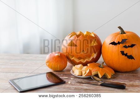holidays, halloween and technology concept - jack-o-lantern or carved pumpkin with tablet pc computer and knife on wooden table at home