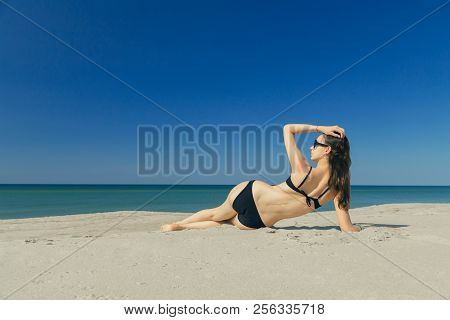 Beautiful Young Woman In Swimsuit At Sand Sea Beach Lying Under Sun Rays Tanning, Toned Image