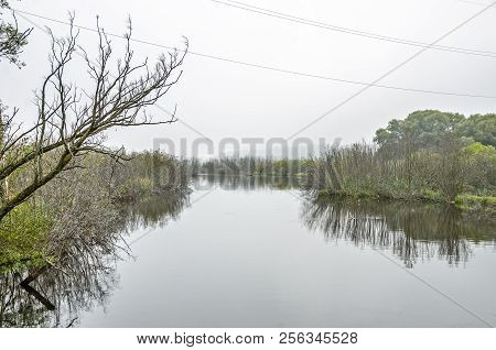 Red Boat On Calm Water On The Manistee River With Fog In The Distance