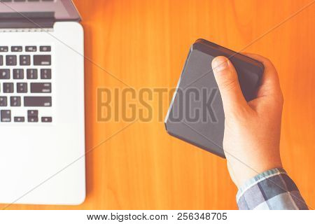 Man Holds Portable External Hard Drive. Laptop On The Table In The Background