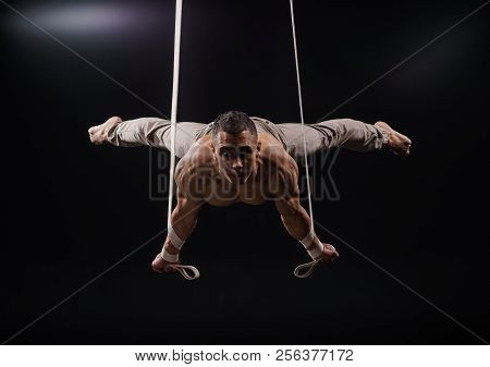 Circus Artist On The Aerial Keeping Planche Straps With Strong Muscles On Black Background