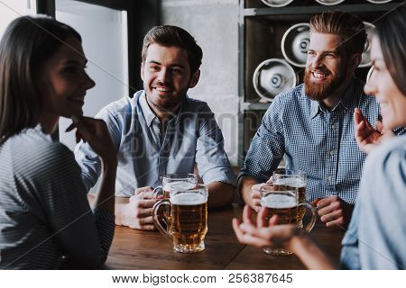 Company Friends Sitting And Drinking Beer In Pub. Happy Friends Drinking Beer And Clinking Glasses A