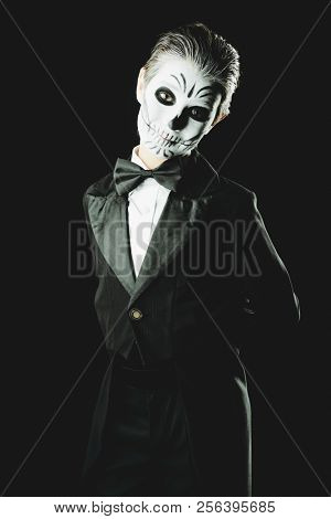 Portrait of a child boy with carnival make-up of a skeleton wearing elegant tail-coat. Studio shot over black background. Halloween. Dia de los muertos. The Day of the Dead.