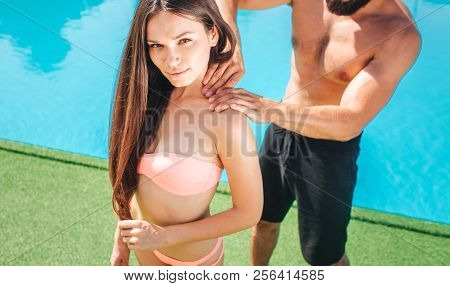 Beautiful Girl Stands At Pool And Looks On Camera. She Smiles. Guy Stands Behind Her. She Is Doing M