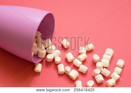White Marshmallow Poured From A Purple Cup On A Pink Background. Close-up