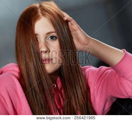 Closeup portrait of attractive young ginger-haired girl looking at camera hand in hair.