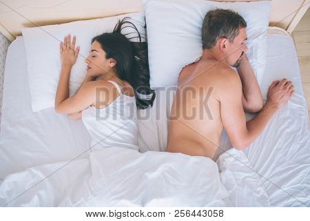 Couple Sleeps In White Bed. Their Faces Look In Different Directions. Girl Keeps One Hand Under Pill
