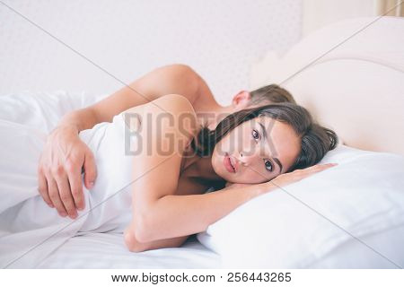Serious Girl Is Lying In Bed And Looks Forward On Camera. She Is Not Sleeping. Bed Is White. Guy Lse