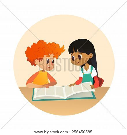 Boy And Girl Reading Book And Talking To Each Other At School Library. School Kids Discussing Story 