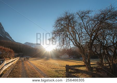 Landscape With The Sun And Its Rays Shining And Warming The Austrian Alps, The Leafless Trees, On A 