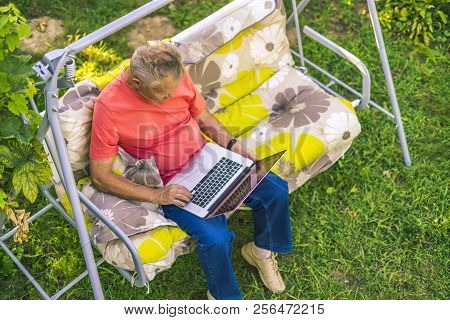Top View Of Eldery Man Sitting And Relaxing On A Summer Holiday Rasort Using Laptop On Grass On Couc