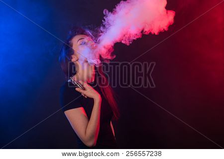 Young Woman In Neon Light And Smoke Of E-cigarettes Or Vape On Dark Background