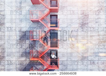 Modern Building Exterior With Concrete Brick Walls, Grey Doors And Red Emergency Exit Stairs. Concep
