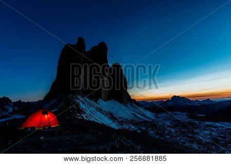 Night bivouac at Tre Cime di Lavaredo, milion star hotel under night sky, red illuminated tent on pass in Dolomites, Italy.