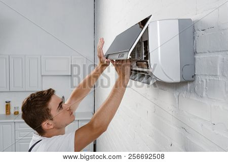 Repairman Taking Off Dirty Filter From Air Conditioner Hanging On White Brick Wall