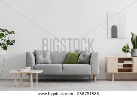 Real Photo Of Grey Lounge With Green Cushion, Wooden Coffee Table, Simple Poster On The Wall And Cup