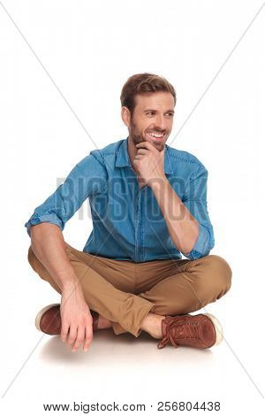 man sitting down laughs and thinks while looking to side on white background