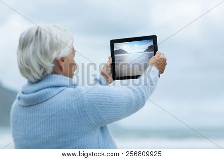 Senior woman photographing scenery using digital tablet on the beach