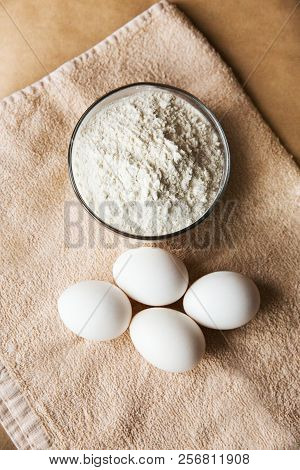 White Chicken Eggs And Bowl Woth Flour On Brown Towel