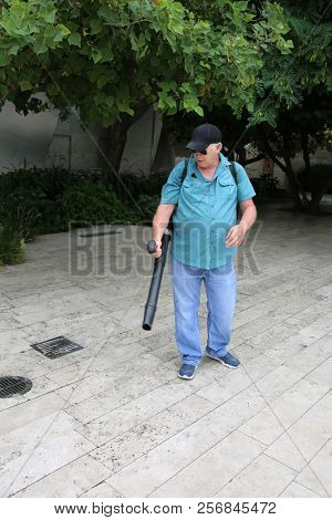 Man uses a Leaf Blower. A man uses a leaf blower to clean up a garden and patio grounds.