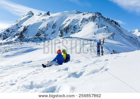 snowboarder and skiier sitting on snow and see at mountains
