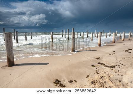 Long Shutter Photo Of Wooden On Sandy Beach With White Clouds And Waves Of The North Sea