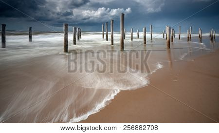 Long Shutter Photo Of Wooden On Sandy Beach With White Clouds And Waves Of The North Sea