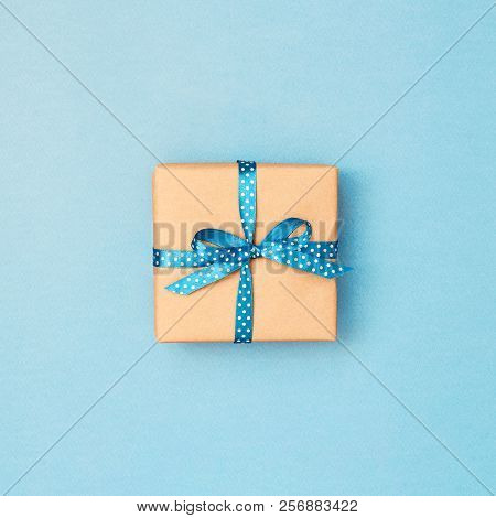 Gift Box Wrapped In Kraft Paper Tied With Blue Ribbon In Polka Dots On Blue Background. Minimal Stil