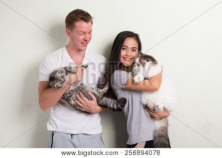 Young Happy Multi-ethnic Couple Holding Two Cats Together Against White Background