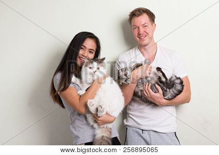 Young Happy Multi-ethnic Couple Holding Two Cats Together Against White Background