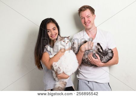 Young Happy Multi-ethnic Couple Holding Two Cats Together Against White Background