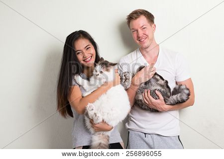 Young Happy Multi-ethnic Couple Holding Two Cats Together Against White Background